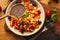 A view of a spelled dish on wooden background with some ingredients around: carrots, peppers, tomatos, parsley and oil