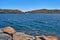 View of Spinalonga island lagoon and Venetian fortress with anchored yacht and breakwater stones in foreground, Crete