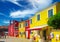 View on square with bright yellow, red colored houses, fashion boutique against clear blue sky, fluffy clouds