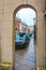 View through a stone arch from a London street to a narrow sidestreet lined by row houses and parked cars on a wet day