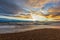 A view of a stony beach at sunset with crashing waves and ecume under a majestic yellow cloudy stormy sky