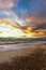 A view of a stony beach at sunset with crashing waves and ecume under a majestic yellow cloudy stormy sky