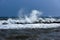 View of a storm at sea with strong winds, high white waves of wild splashing water, and a dark threatening sky.