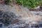 A view of the stormy flow of clear water from the culvert on a bright summer day