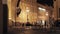 View street with illuminated buildings, watch, fence and people in night.