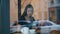View from the street of a young woman drinking tea or coffee from the white cup in cafe sitting in the coffee shop by