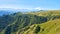 View of the sun-drenched green hills stretching in front of the peaks of Elbrus.