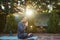 View through the sunset sunlight falling on the backyard, to a peaceful man yogi meditating in lotus pose on a yoga mat