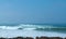 View of swirling waves in Atlantic Ocean and blue clean sky on horizon. Seascape. Rocks and headland on the foreground