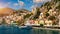 View on Symi (Simi) island harbor port, classical ship yachts, houses on island hills, Aegean Sea bay.