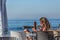 View of technological senior woman taking sunbath on beach club, sea as background, in Portugal