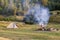 View with a tent, camping fire wit smoke and tourist hiker in summer day.