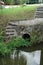 View of a tiny water tunnel with stairs above in the field with plants and trees