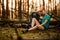 View of tired young woman in forest who is sitting near fallen tree