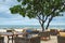 View to Alfresco cafe with cozy rattan furniture and plumeria tree on ocean beach terrace.