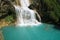 View to amazing waterfall with turquoise pool surrounded by green rocks and a faint rainbow