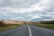 View to the empty curvy road, empty meadow and red mountains in the background in Myvatn region,