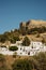 A view to a little village Lindos on a hill which is full of white houses located in Rhodes, Greece. An old castle on the backgrou