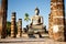 View to the ruins and sitting Buddha statue at Wat Mahathat temple in Sukhothai Historical Park