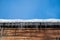 View to the wooden wall and snow roof of house with icicles and blue sky.