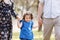 View on toddler. Mother, father hold hands daughter enjoy nature and walk in spring park. Young family spending time together on