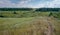 A view from the top of a hill on a rural landscape of a meadow with hills and vales cut with dirt footpaths. Blue summer sky with