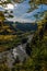 View from the top of a river where little water flows, during a sunny fall day. Some branches and leaves tending to autumnal hues