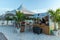 View of tourists in line for drinks in outdoor bar. White sand coast and palm plants on blue sky background. Oranjestad. Aruba.