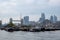 View of Tower Bridge and tall City buildings in the background. In the foreground are houseboats at Shad Thames.