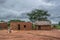 View of traditional village, thatched houses on roof and terracotta brick walls, kids playing outside, cloudy sky as background