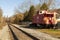 View of the train tracks, ballast, track sleepers and an abandoned red caboose passenger train cabin