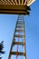 View from under an aluminum extension ladder, looking up towards roofline and blue sky