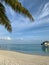 A view from under the branches of a palm tree to the coast of the Indian Ocean with white sand, azure water, in which a villa