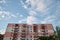 View from underneath on colorful pink apartment building in front of blue sky with clouds. City dwelling. Urban architecture