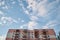 View from underneath on colorful pink apartment building in front of blue sky with clouds. City dwelling. Urban architecture