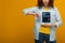 View of upset curly woman holding digital tablet with booking app on screen and showing thumb down on orange