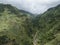 View of valley with green mountains and tropical plants, road and stream from hiking trail Levada do moinho to levada