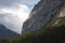 View on the valley and  rock wall. Sunbeam behind the clouds. Forest below. High alpine mountains cloud scape. Switzerland.