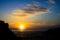 View on vibrant yellow golden orange sunset over atlantic ocean with silhouette of rocks and clouds, sunburst effect