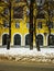 View of the wall of yellow house with arched beautiful windows through the trees and with a dirty road in snow in winter