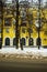 View of the wall of yellow house with arched beautiful windows through the trees and with a dirty road in snow in winter