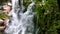 View from the water of cascading waterfall as it falls down into a natural pool surrounded by lush rainforest.