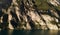 View from the water to a rocky mountain with vegetation, with tunnels and roads at the very edge of the water