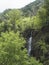 View of waterfall at levada, water irrigation channel and tropical plants from hiking trail Levada do moinho to levada