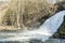 View of a waterfall with a rainbow reflected in the water with an arid vegetation in the background in the small city of Spa Belgi