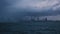 View of wavy sea and city buildings and lights on a dramatic gloomy day.