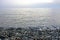 View of wavy seascape and blue sky from beach with pebbles on it.