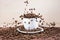 View of white cup standing on white plate with roasted coffee beans on tablemat.