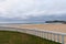 View of white fence on a deserted beach, a cloudy afternoon, with the sea in the background and the green coast, in Comillas, Cant