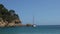 View of a white sailboat anchored on mediterranean sea near rugged rocky coast